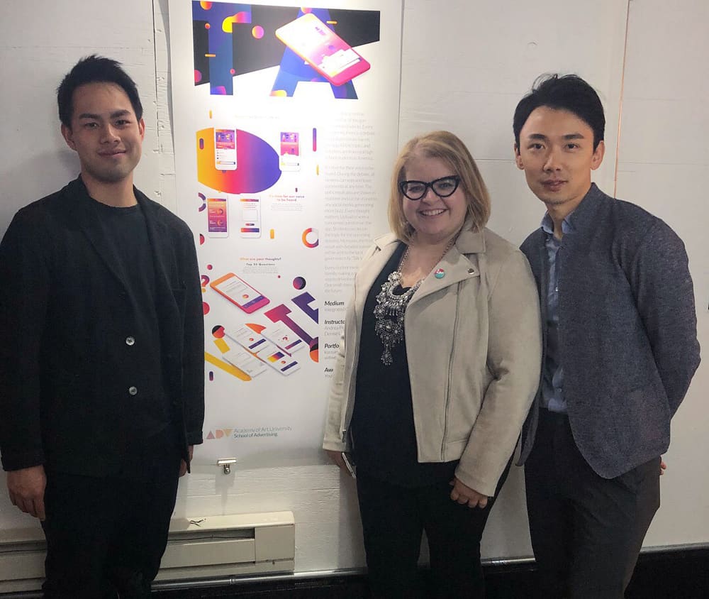 School of Advertising alumni Hsiu Chi (Sam) Kuo and Wei (Will) Wang with Advertising and Interaction & UI/UX Design Co-director Andrea Pimantel (center). They're standing before a project awarded in the Young Glory advertising competition.